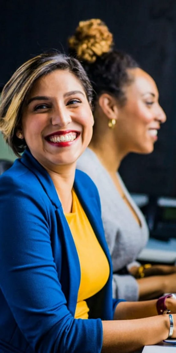 woman working on laptop while smiling a co-worker
